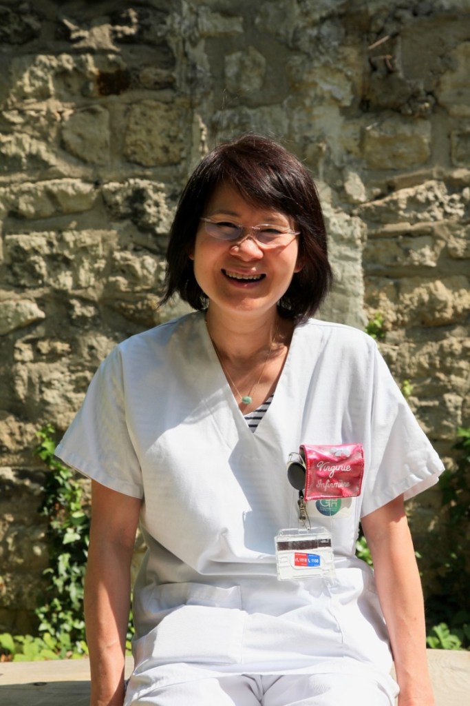 Photographie de Virginie, infirmière. Elle est dehors, au soleil, en blouse de soignante, et sourit
