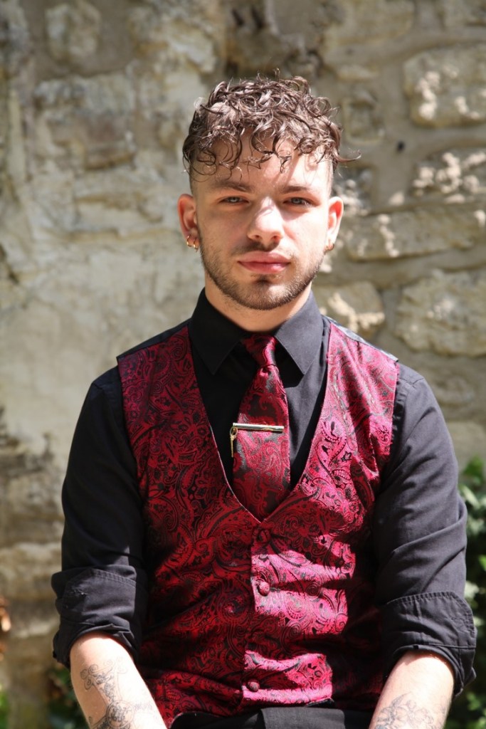 Photographie de Juan, agent d'amphithéâtre. Il est dehors, au soleil, habillé élégamment et regarde l'objectif